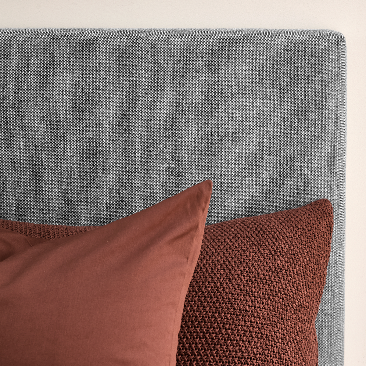 Grå textil sänggavel med två rostbruna kuddar.