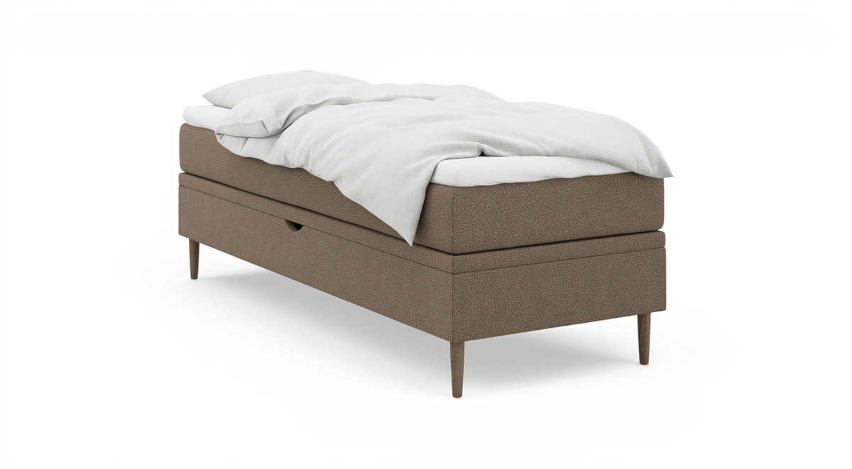 Enkel säng med beige klädsel, träben och vit bäddning, frilagd.