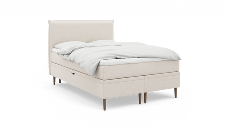 Beige kontinentalsäng med vitt bäddset och träben, frilagd snett framifrån.