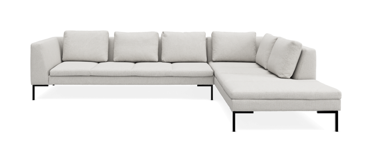 Ljusbeige L-formad modulsoffa med chaiselong till höger, på slanka svarta ben, frilagd mot vit bakgrund.