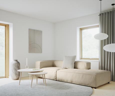 Ljust vardagsrum i skandinavisk stil med beige modulsoffa, två runda vita soffbord, stor keramikvas, grå rund matta, väggkonst, gardiner och två hängande rislampor vid fönster i dagsljus.