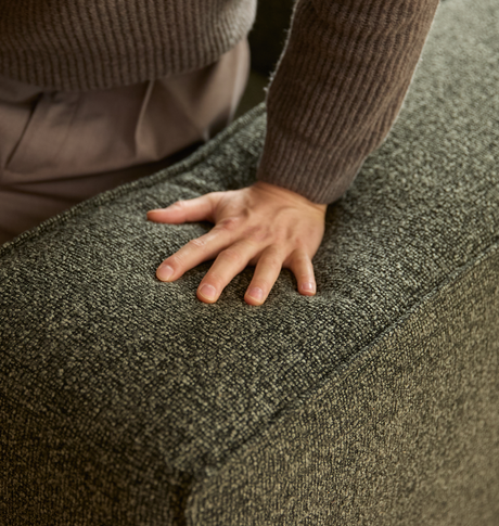 Hand som trycker på en grönt melerad soffa i grov, mjuk textil.
