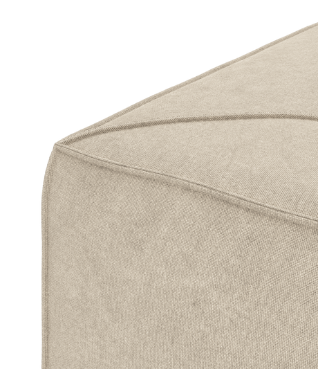 Närbild av hörnet på en beige textilpuff med synliga sömmar.