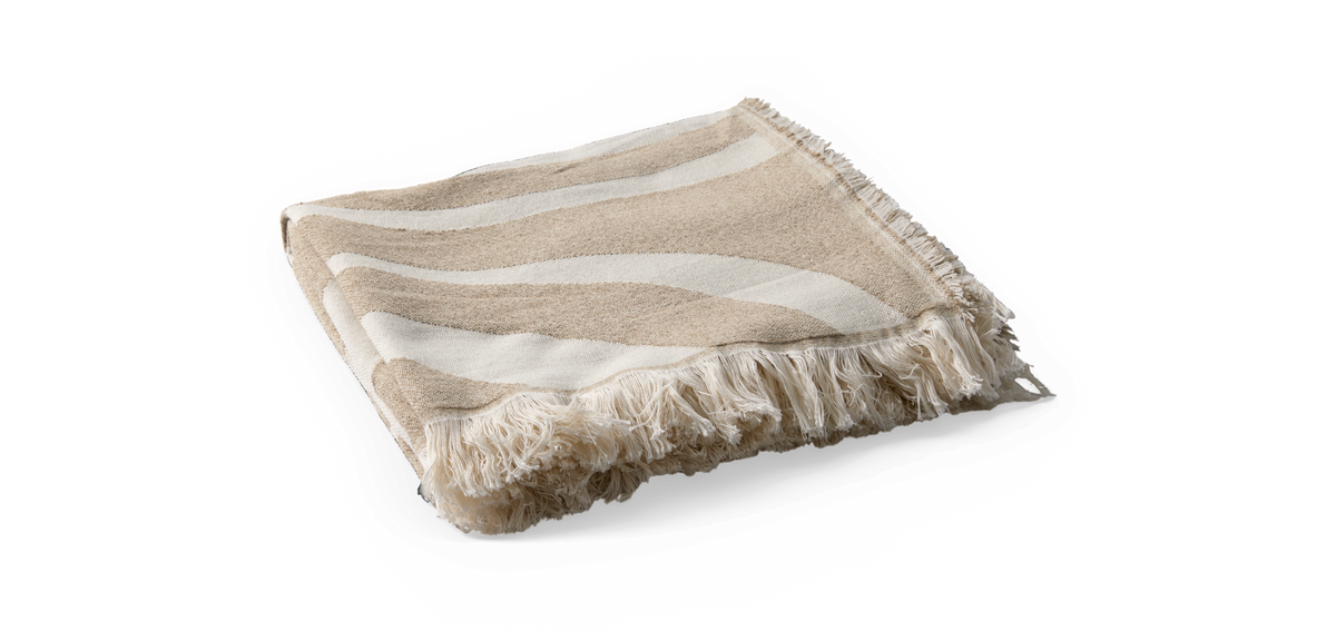 Beige och vit pläd med vågiga ränder och fransar, hopvikt.