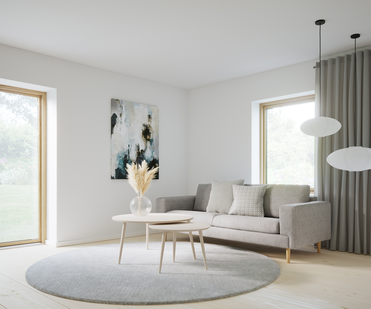Ljust skandinaviskt vardagsrum med grå soffa, runda ljusa soffbord, vas med pampasgräs, abstrakt väggkonst, två vita pendellampor och stora fönster med gardiner över en mjuk rund grå matta.