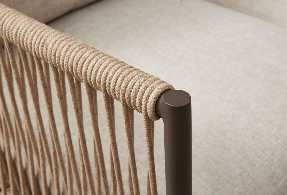 Närbild av flätad repdetalj runt brunt metallarmstöd med beige klädsel i bakgrunden.