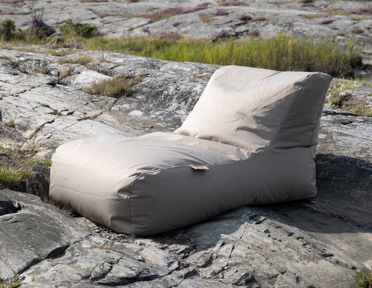 Beigefärgad loungestol i sittpuff/beanbag-stil placerad på klippor utomhus.