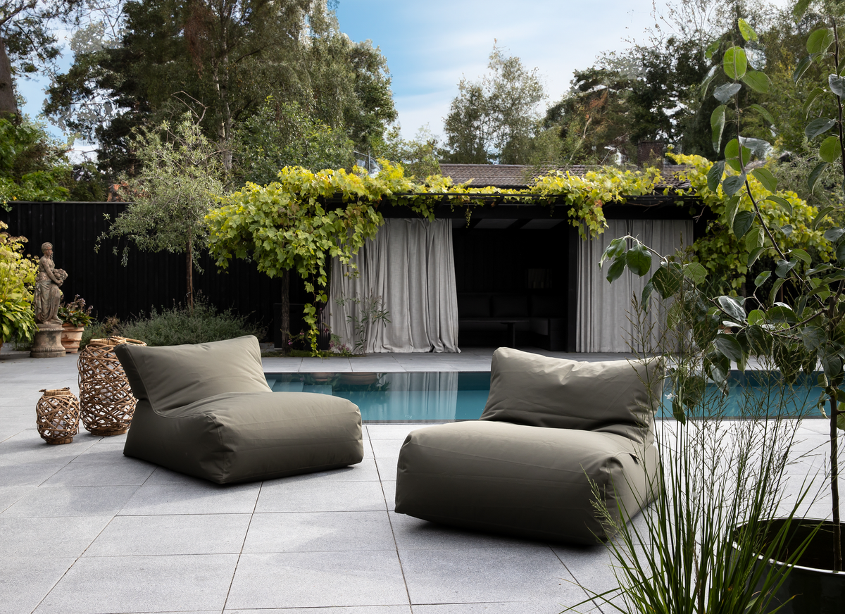 Uteplats med två olivgröna loungestolar vid en pool, flätade lyktor och pergola med ljusa gardiner i dagsljus.