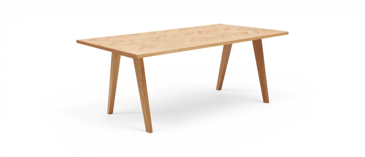 Rektangulärt matbord i ljus ek med fiskbensmönstrad bordsskiva, frilagt mot vit bakgrund.
