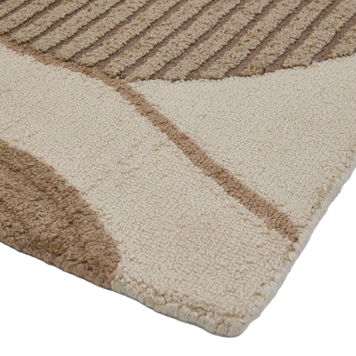 Närbild av ett hörn på en beige och brun matta med geometriskt och räfflat mönster och mjuk lugg.