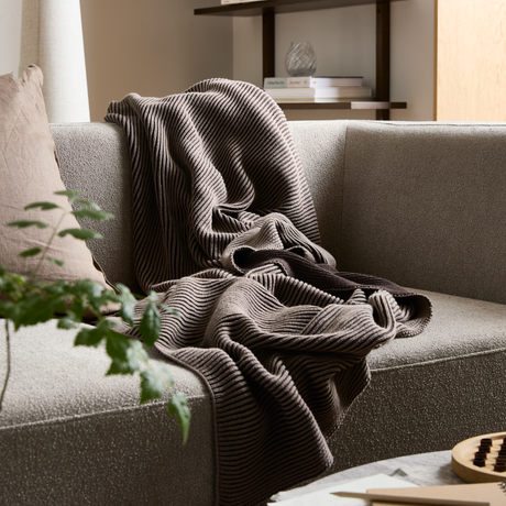 Beige soffa med ribbad brun pläd och kudde i ett lugnt vardagsrum.