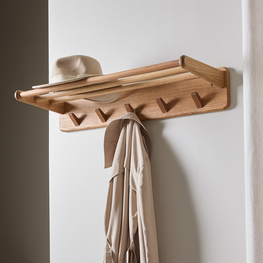 Väggmonterad klädhängare i trä med hylla, beige hatt ovanpå och beige rock som hänger.