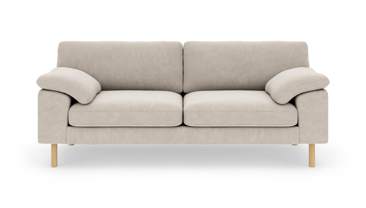Beige tvåsits soffa med lågprofilarmstöd, lösa sits- och ryggkuddar och ljusa träben, frilagd mot vit bakgrund.