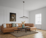 Ljust vardagsrum med brun lädersoffa, svarta soffbord, pampasgräs i grön vas, modern pendellampa och väggpaneler vid fönster i dagsljus.