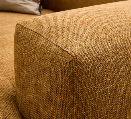 Närbild av senapsgul vävd textil på soffans armlän med beige kudde i bakgrunden.
