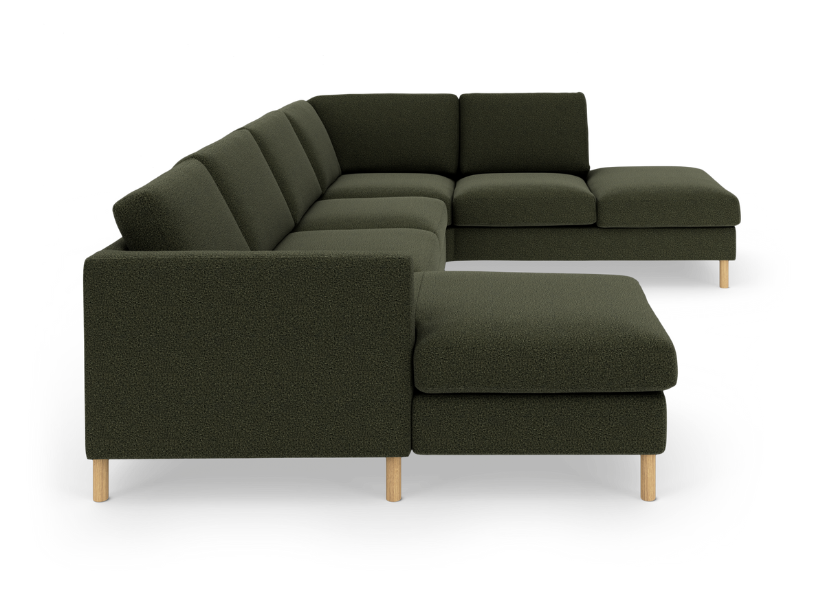 Mörkgrön modulsoffa i U-form med schäslong och ljusa träben, frilagd på vit bakgrund.