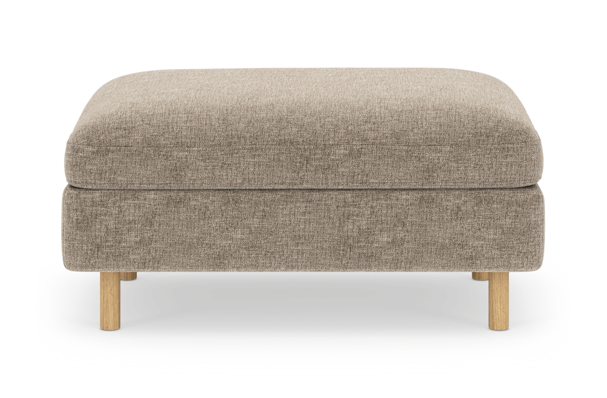 Beige tygklädd ottoman/puff med rundade hörn och runda ben i ljust trä, centrerad på vit bakgrund.