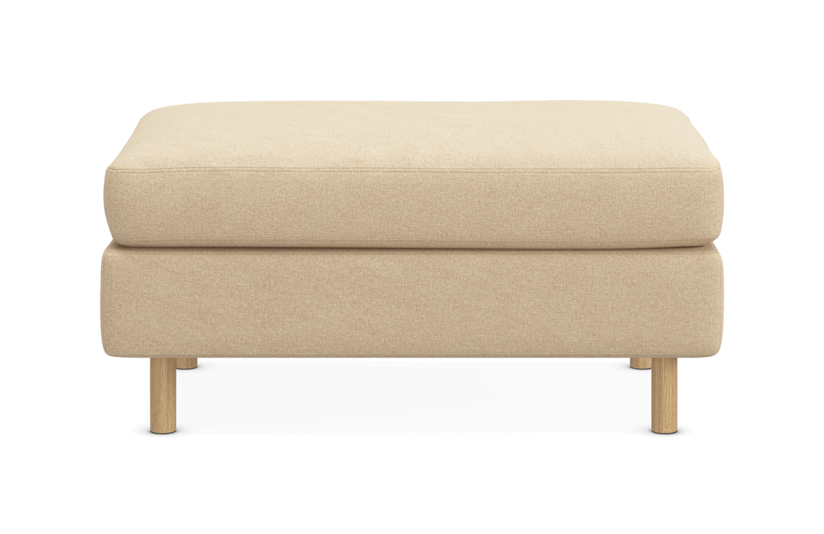 Beige fotpall med textilklädsel og ljusa träben, fotograferad rakt fram mot vit bakgrund.