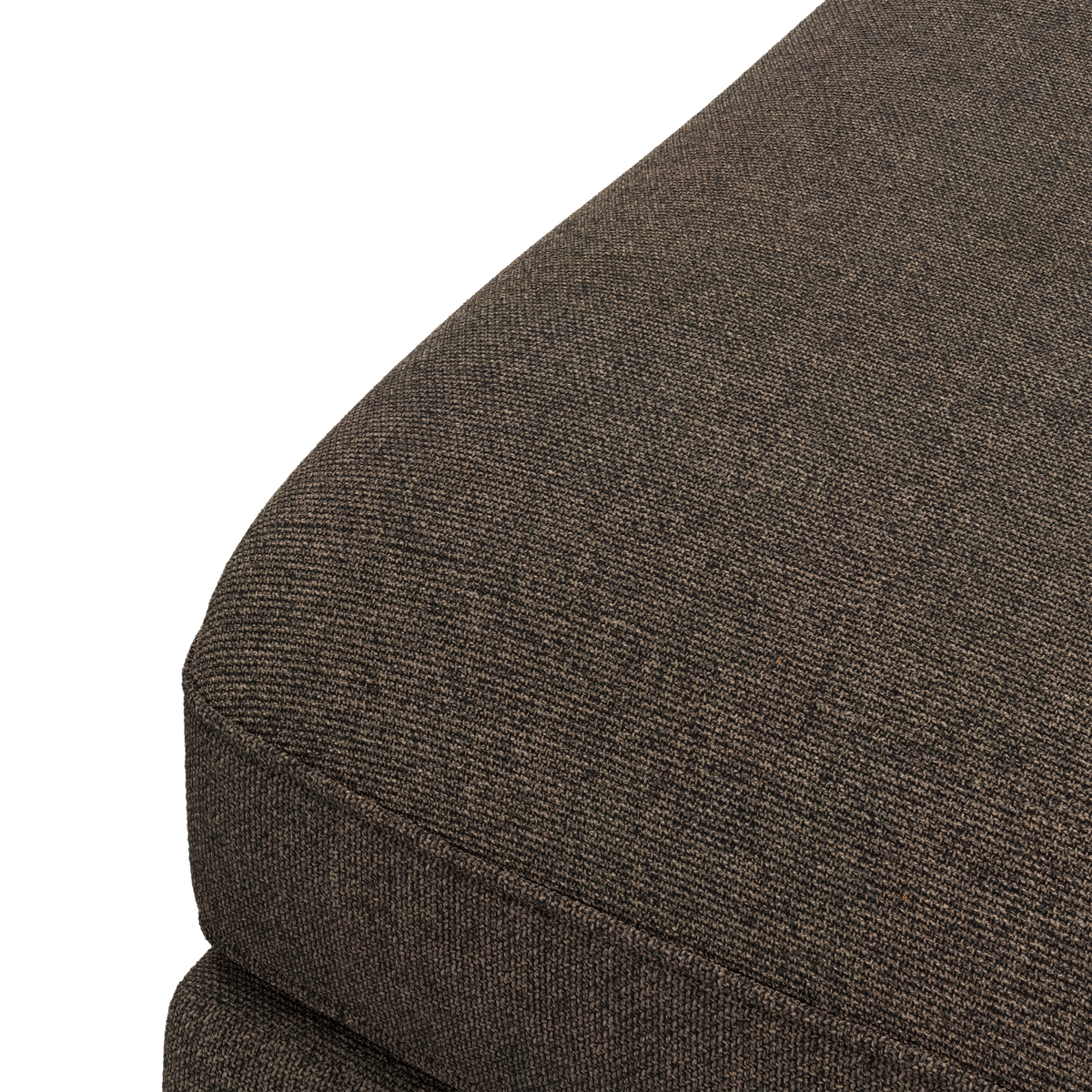 Närbild av mörkbrun, melerad textil på sittdyna till soffa mot svart bakgrund.