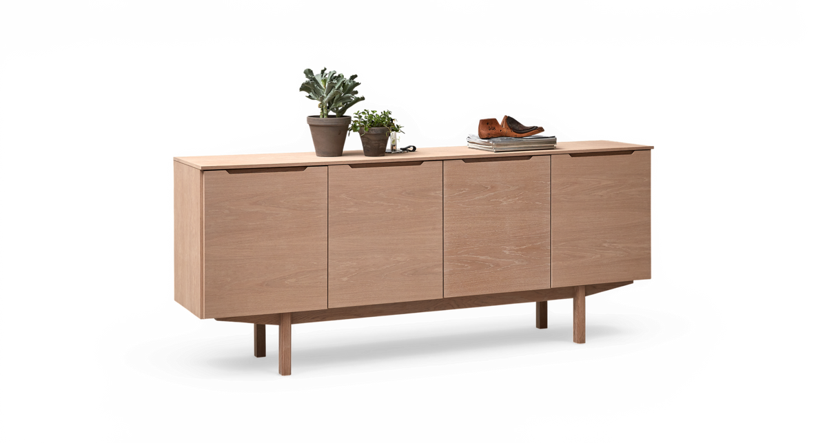Ljus träsideboard med fyra dörrar, växter i krukor, böcker och ett par bruna skor ovanpå, frilagd mot vit bakgrund.