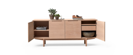 Ljus ekfärgat sideboard med öppna dörrar, hyllor och låda; böcker, växter, ljus och skor ovanpå samt flätad korg inuti.