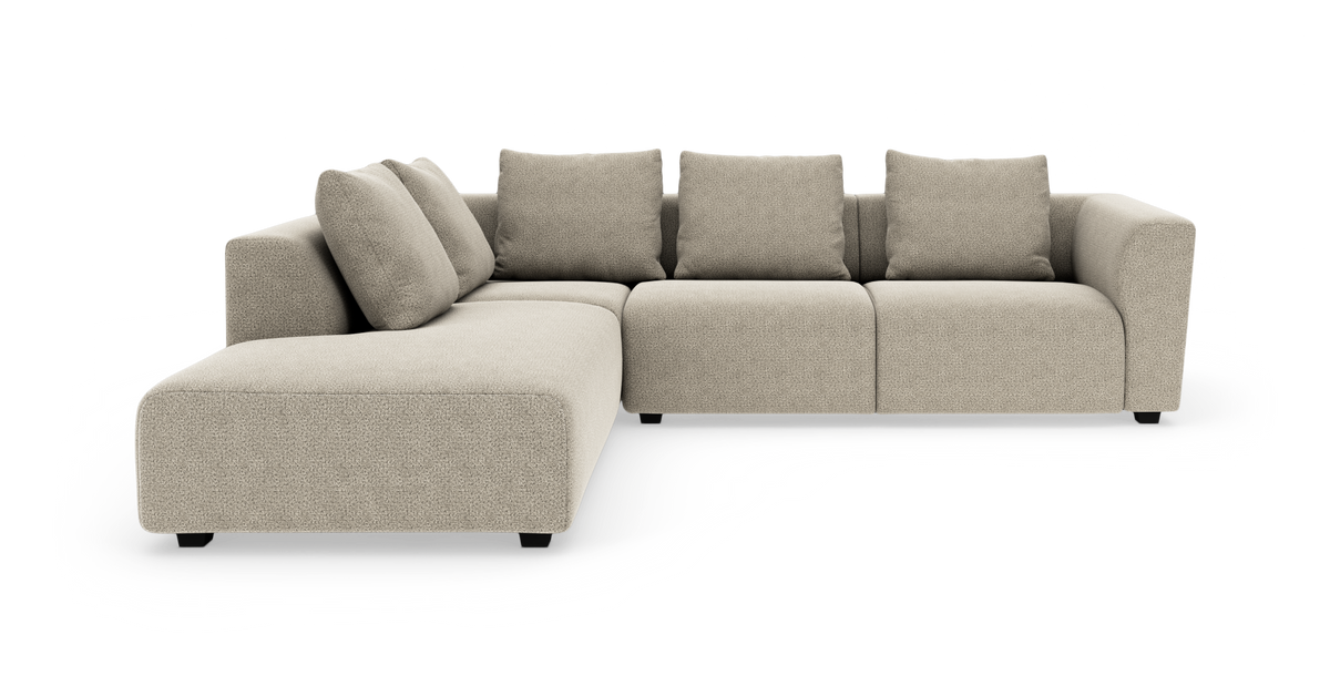 Beige L‑formad modulsoffa med schäslong och fyra kuddar, sedd framifrån i studiobelysning.