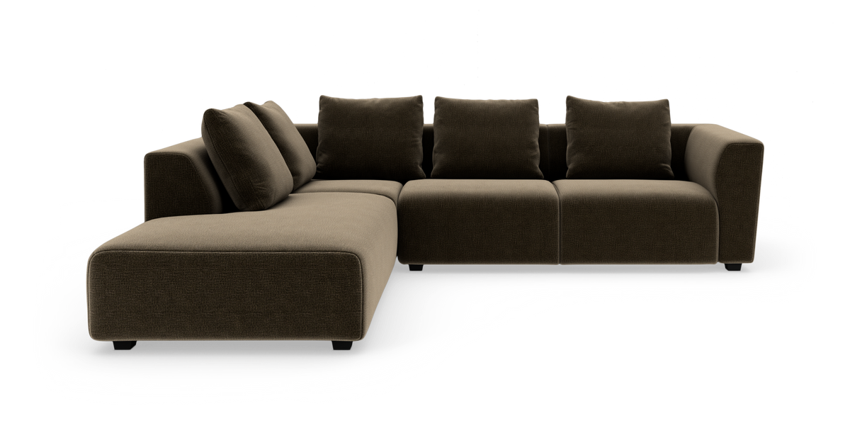 Modulär L‑soffa i mörkbrunt tyg med vänster schäslong och fyra ryggkuddar, modern låg design i studioljussättning.