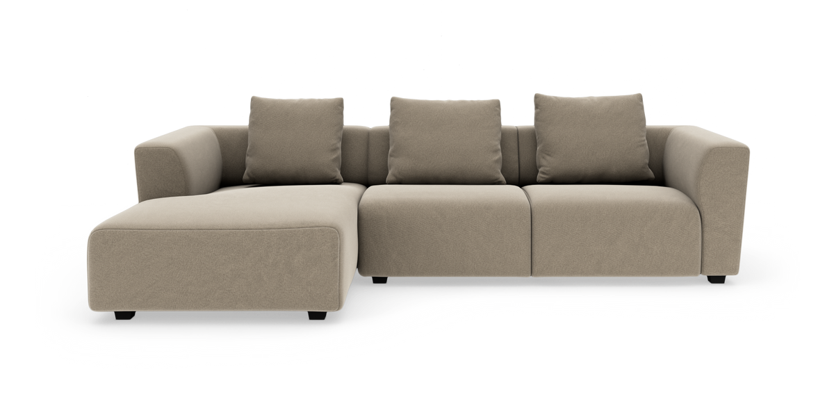 Beige modulsoffa med vänstervänd divan, tre sittplatser och fyra ryggkuddar på vit bakgrund.