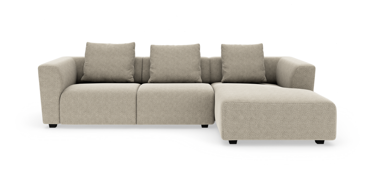 Beige modulsoffa med schäslong till höger, tre sittplatser och fyra kuddar, modern mjuk form mot vit bakgrund.