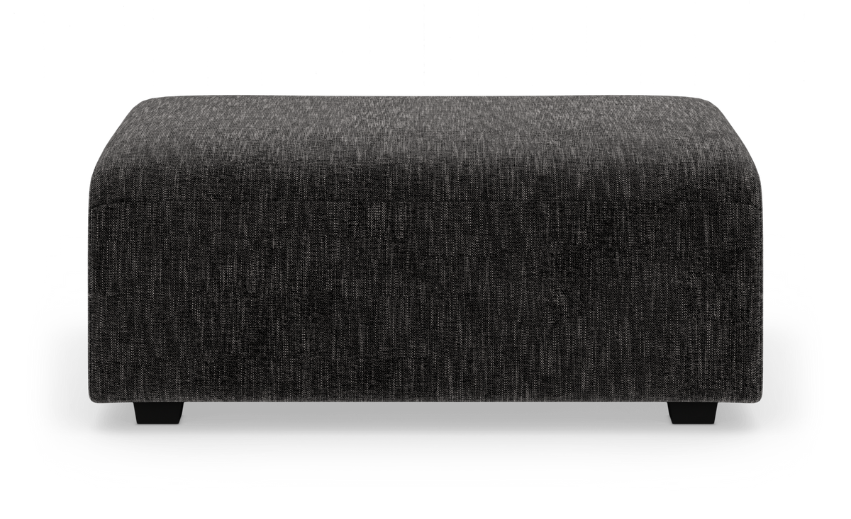 Mörkgrå rektangulär sittpuff/ottoman i tyg på vit bakgrund.