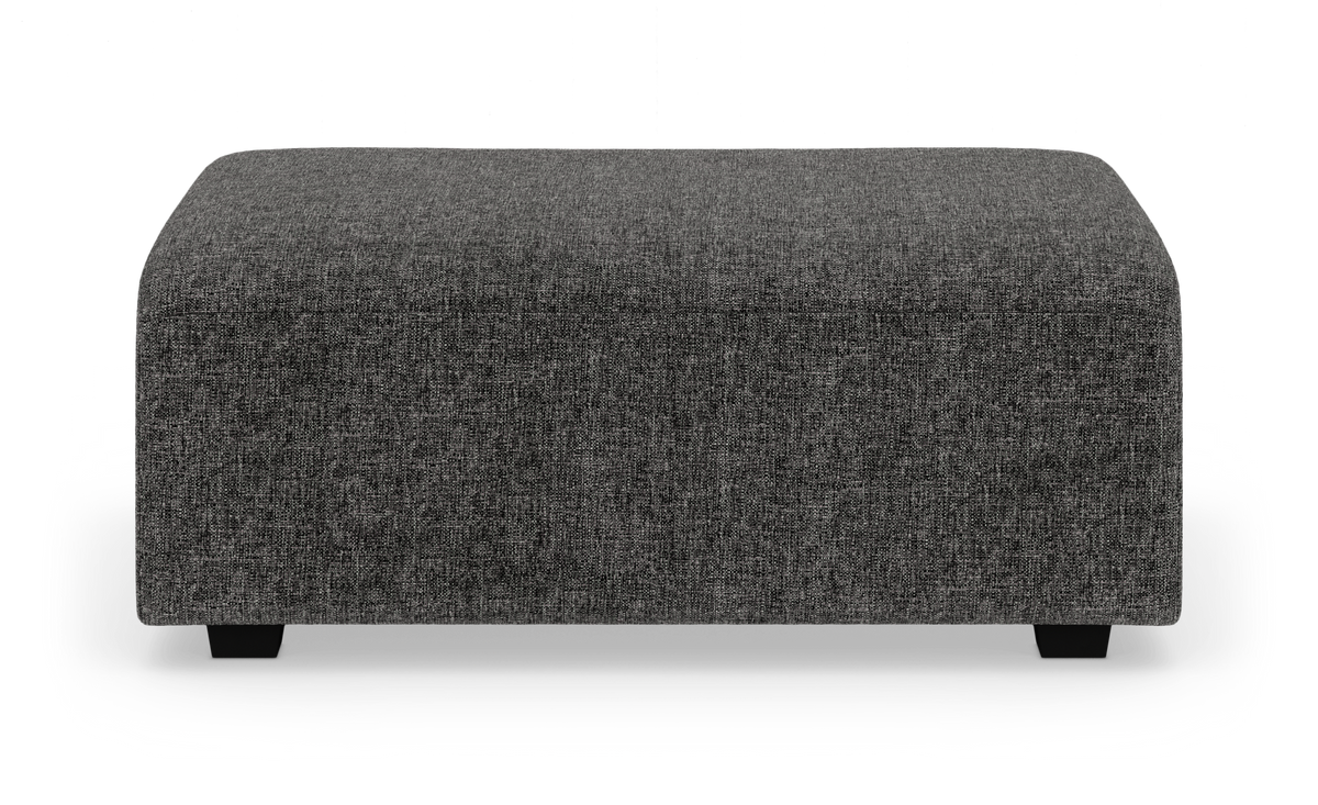 Mörkgrå rektangulär sittpuff/ottoman i tyg på vit studiobakgrund.
