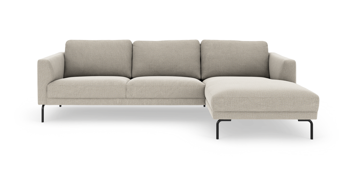 Beige L-formad soffa med schäslong till höger på smala svarta metallben, sedd rakt framifrån.