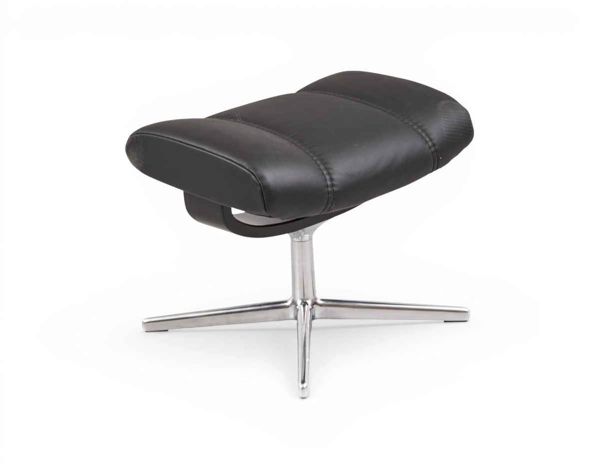 Svart läderfotpall med kromat fyrkryssat stativ, frilagd på vit bakgrund.