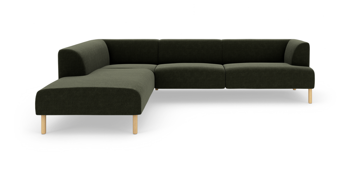 Mörkgrön L-formad modulsoffa med rundade hörn och ljusa träben, frilagd mot vit bakgrund.