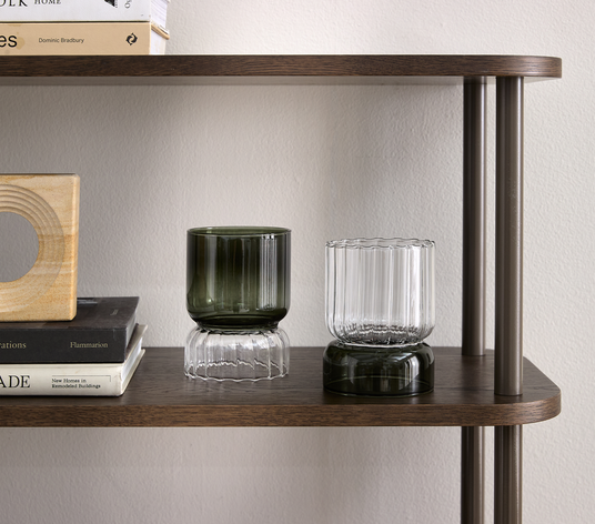 Mörk trä-hylla med två räfflade glasvaser/ljuslyktor i klarglas och olivgrönt, placeret/staplade i tvådelad form, ved siden av böckerna Flammarion, New Home in Remodelled Buildings och en titel av Dominic Bradbury.