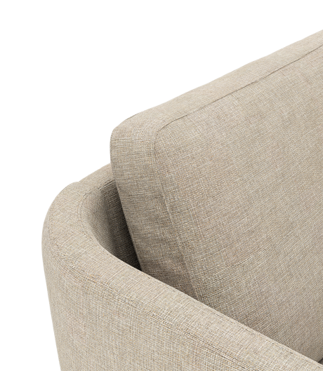Närbild av beige tygsoffa med rundat armstöd och lös ryggkudde, frilagd mot svart bakgrund.