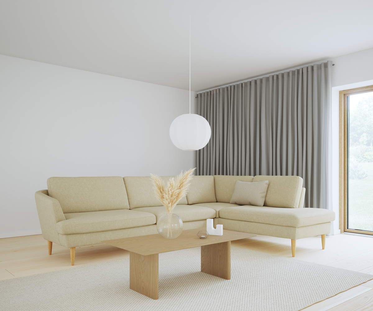 Ljust skandinaviskt vardagsrum med beige hörnsoffa, träbord med pampas i glasvas, rund vit pendellampa och grå gardiner vid stort fönster.