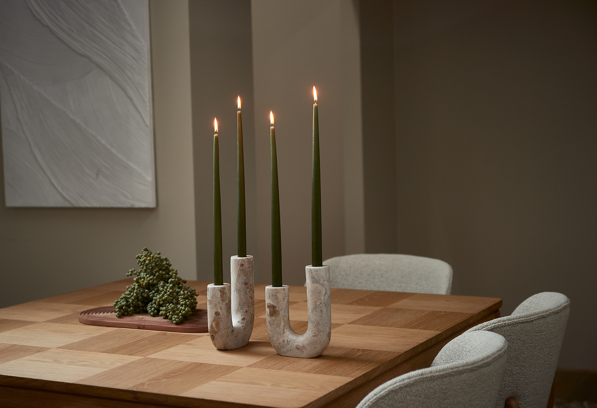 U-formade ljusstakar i sten med fyra tända gröna kronljus på ett träbord i en neutral, minimalistisk matsal.