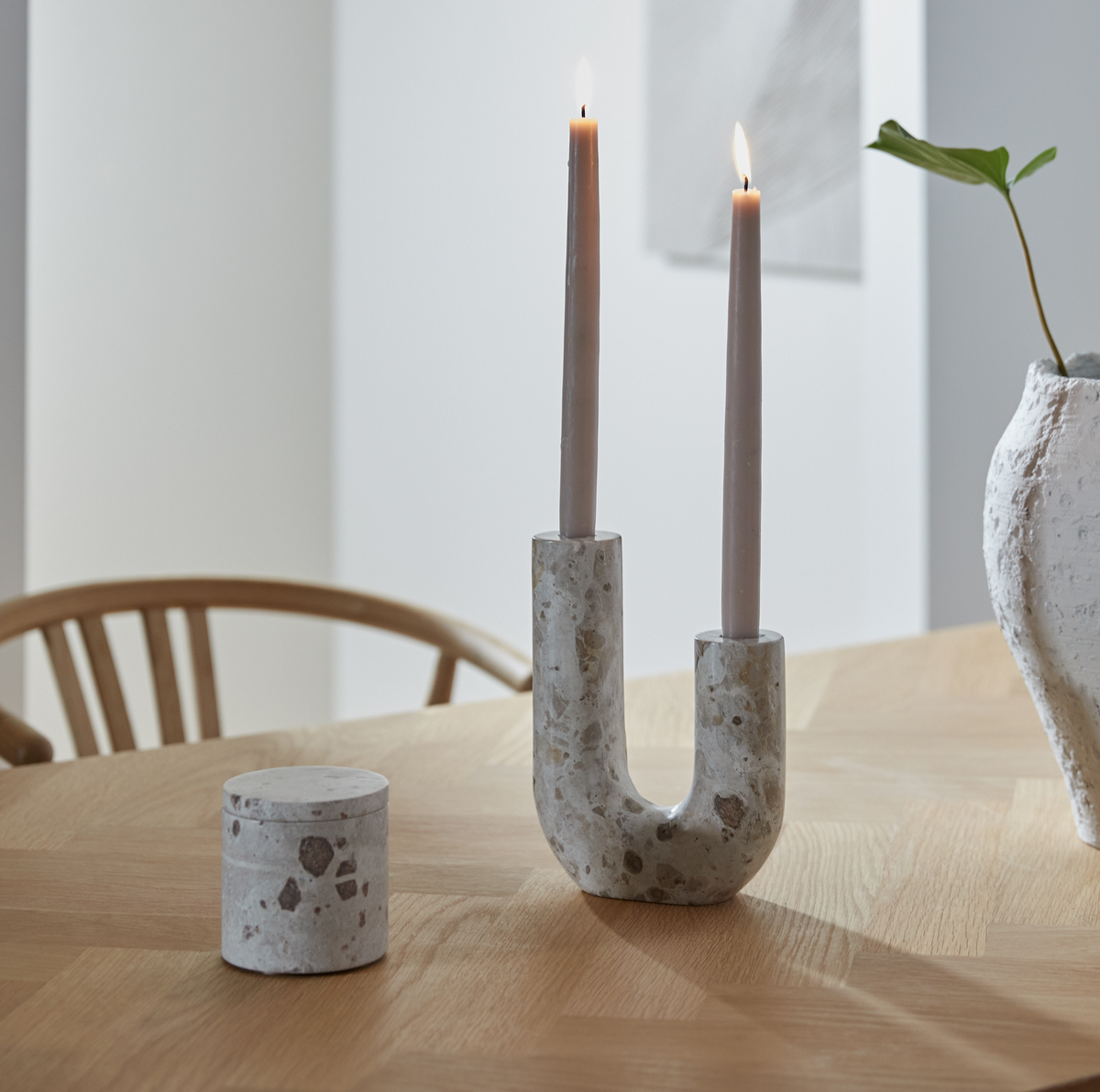 U‑formad ljusstake i terrazzo med två tända ljus på träbord, liten rund burk och en vit vas bredvid.