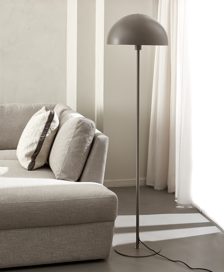 Modern golvlampa med kupolskärm bredvid beige soffa i ljust vardagsrum med vita gardiner.