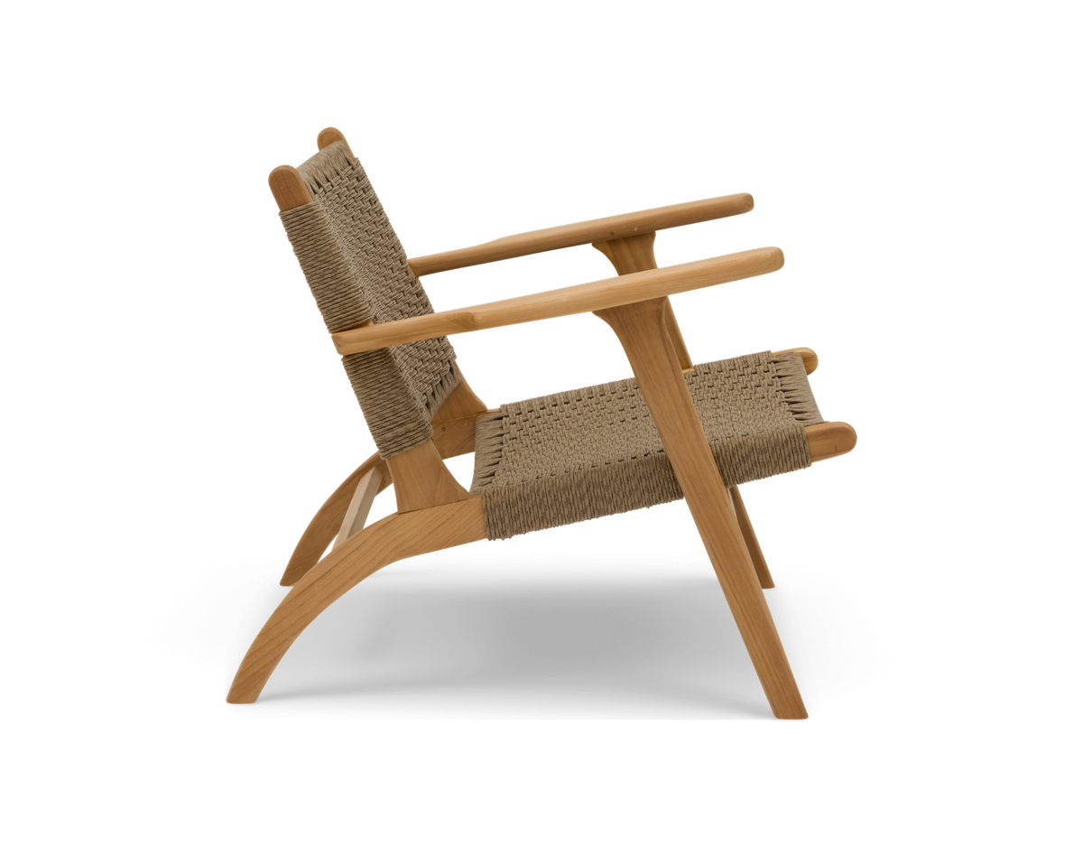 Låg loungestol i ljust trä med flätad sits och ryggstöd, sidovy mot vit bakgrund.