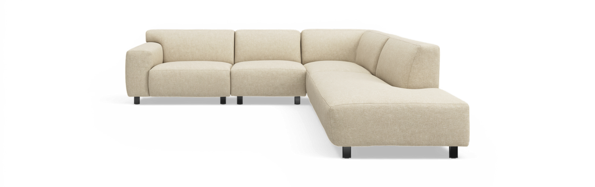 Beige L‑formad modulsoffa i tyg med rundade hörn och svarta ben, frilagd mot svart bakgrund med högerställd hörnsektion.