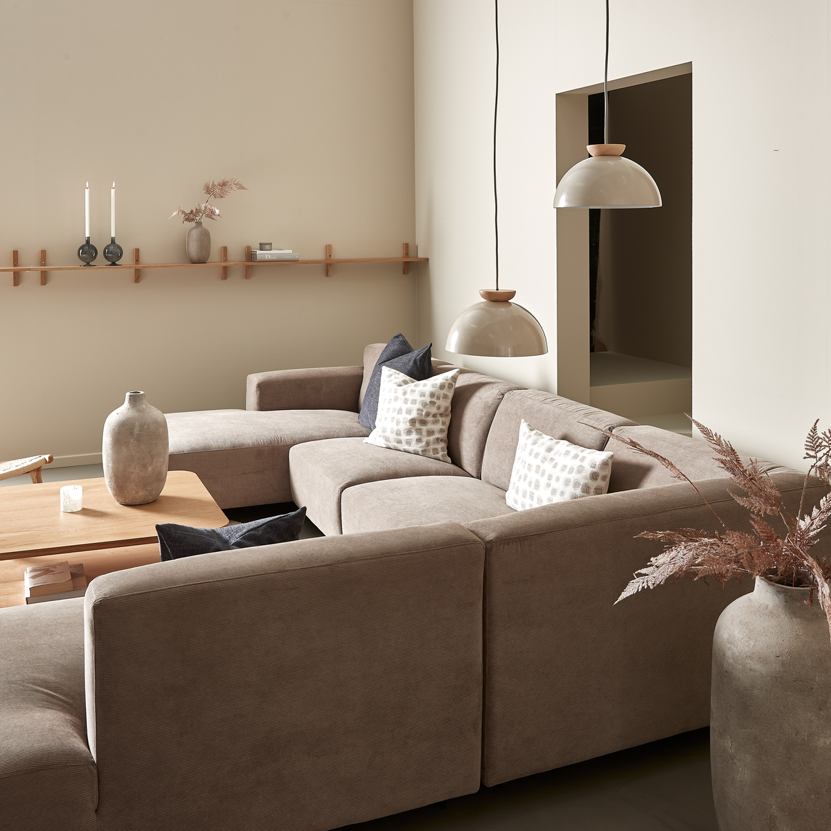 Beige vardagsrum med modulsoffa, träbord, två kupolformade pendlar och keramikvaser i neutrala toner.