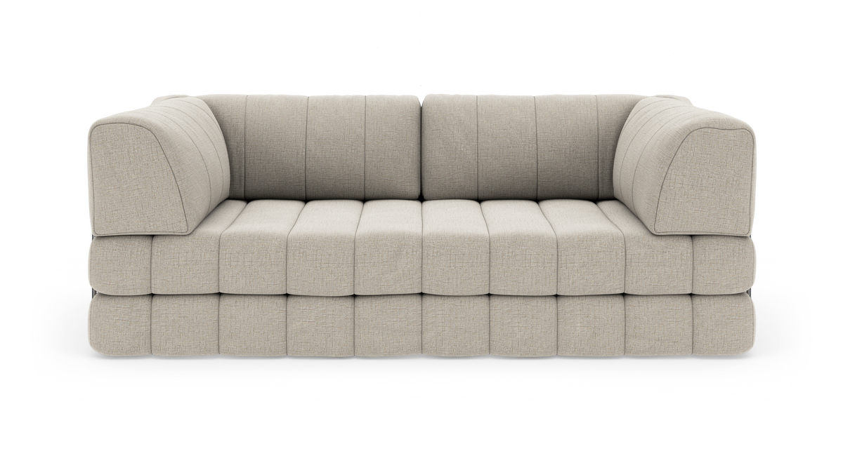 Beige modulsoffa i tyg med mjuka kanter och quiltad sits, fotograferad rakt fram mot vit bakgrund.