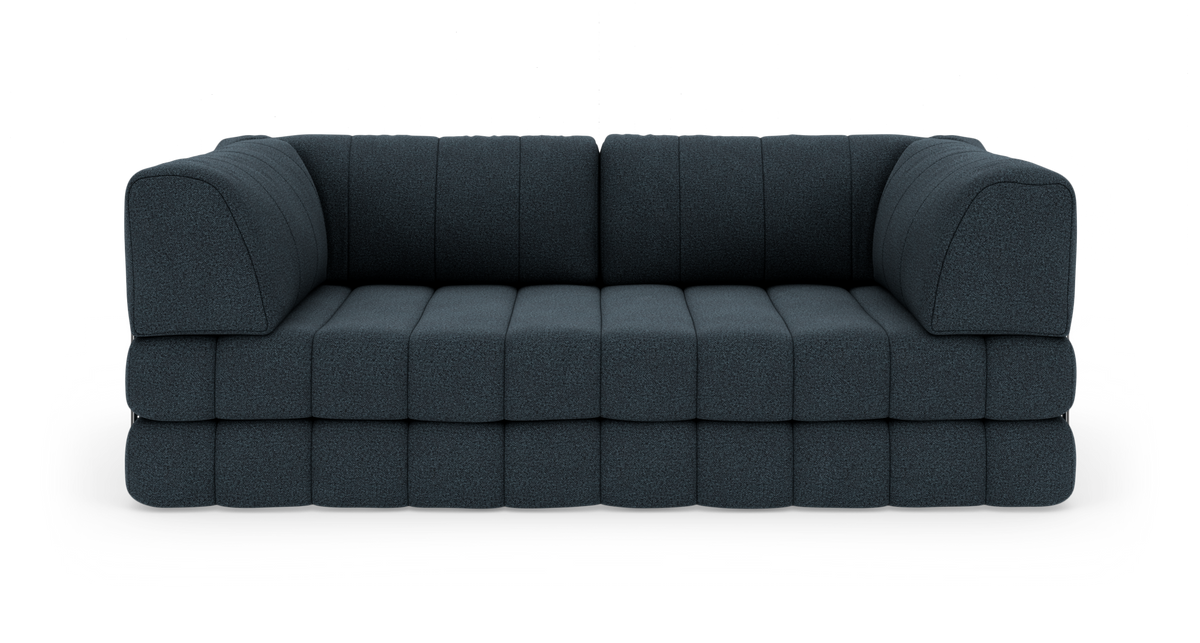 Modulsoffa i mörkblått tyg med låga, breda sittdynor, fotograferad rakt fram mot vit studiobakgrund.