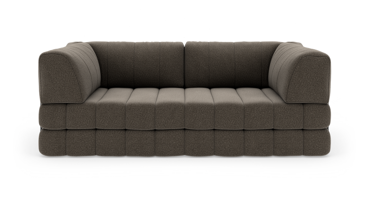 Modulsoffa i mörkgrå/brun textil med djupa kviltade säten och rundade armstöd, frilagd på vit bakgrund.