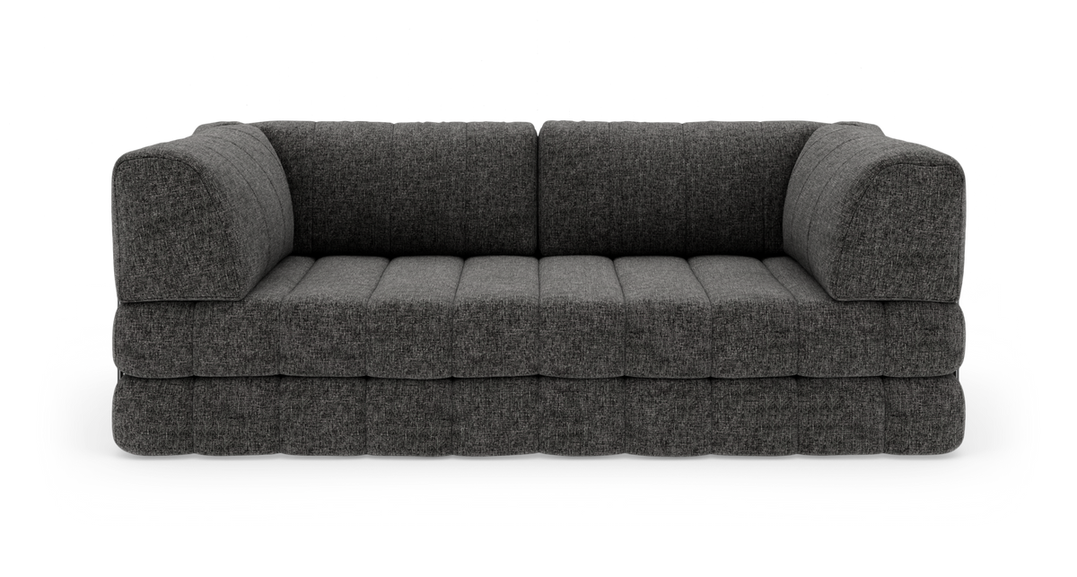 Mörkgrå modulsoffa med mjukt rundade armstöd och quiltad sits, frilagd mot vit bakgrund.