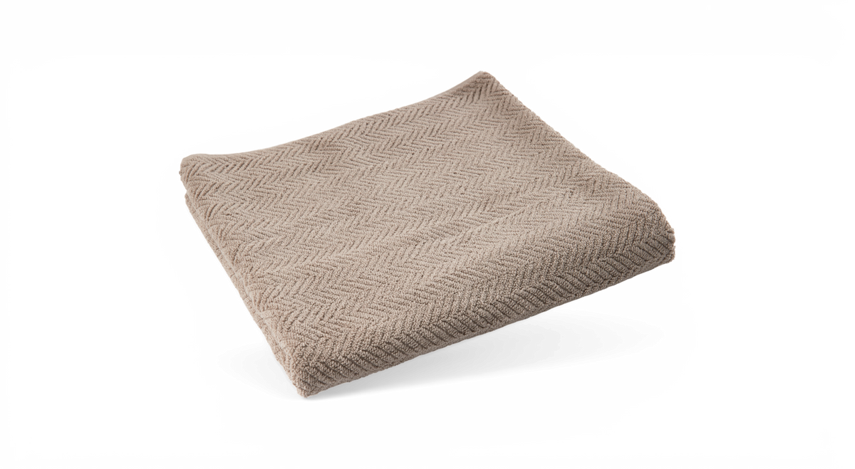 Beige handduk med fiskbensmönster, vikt platt på vit bakgrund.