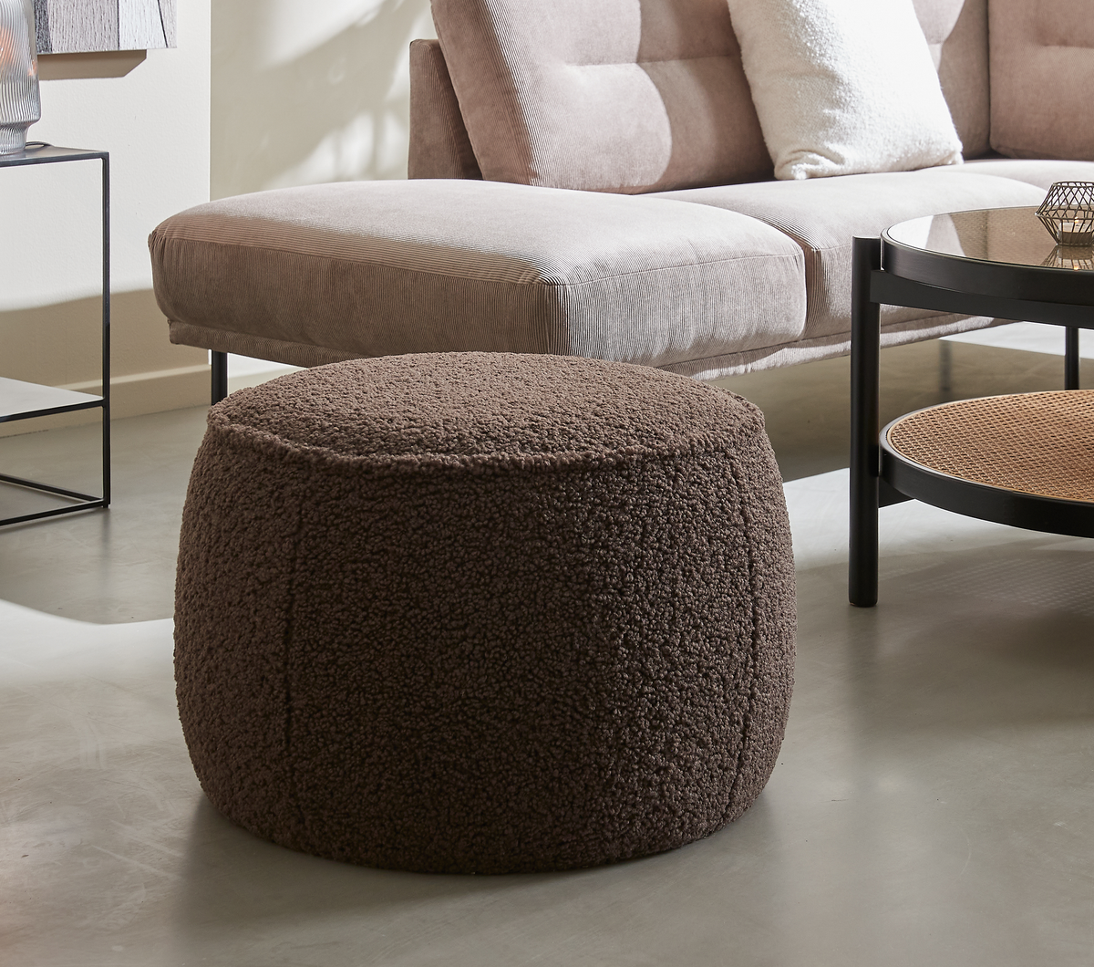 Brun rund bouclé‑puff framför en beige soffa och runt soffbord i ett ljust vardagsrum.