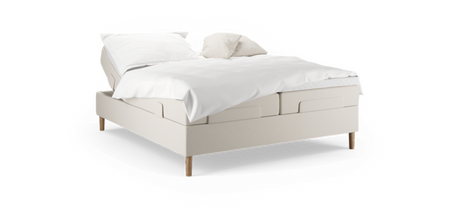Beige justerbar säng med vita sängkläder och två kuddar, träben, frilagd mot svart bakgrund.